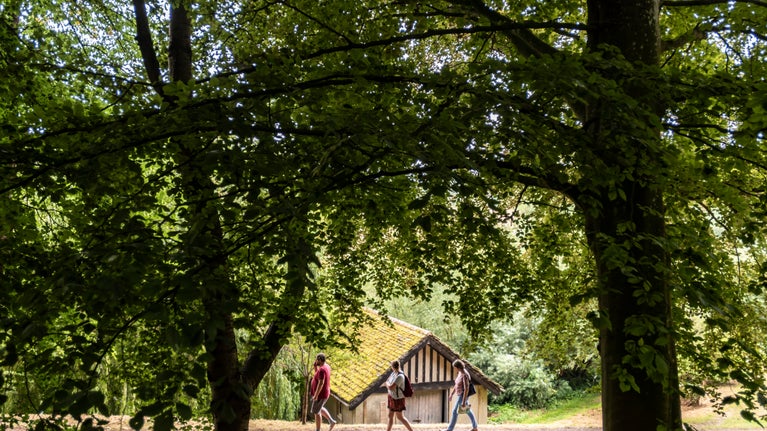 A long distance shot of two visitors walking past the boathouse in the garden.